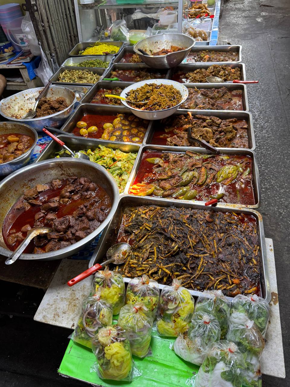 Street food stall in Bangkok — multiple Thai dishes in metal trays, 40–60 THB per portion